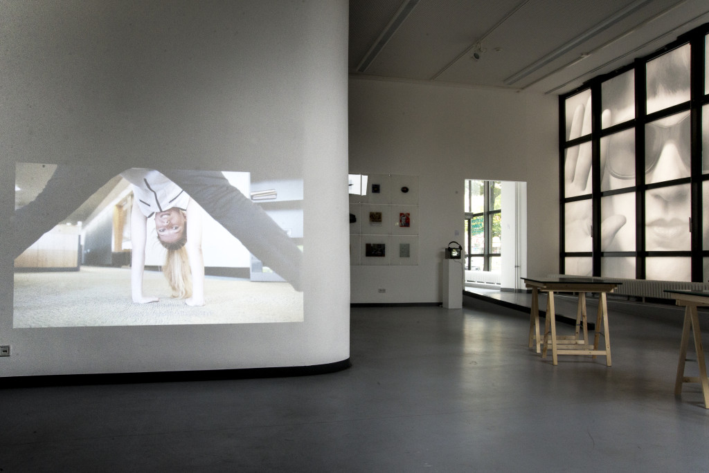 Einen Teil der Ausstellung bildet eine audiovisuelle Installation im vorderen Teil des Raumes, welche auf eines der weißen Galeriewände projiziert wird.