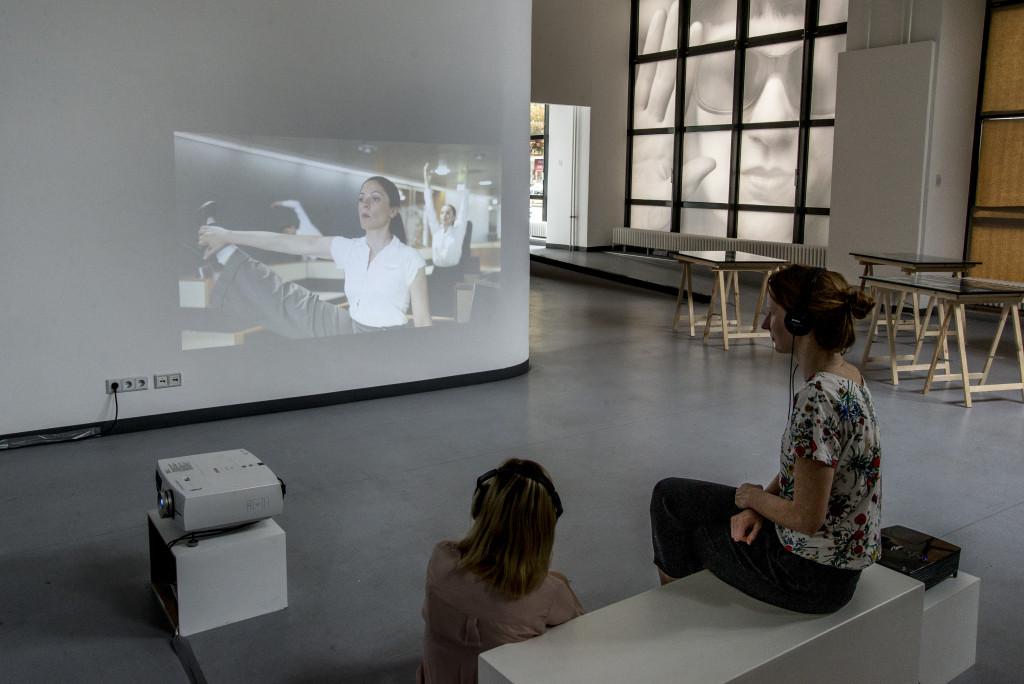 Zwei Besucherinen betrachten mit aufgesetzten Kopfhörern die audiovisuelle Installation.