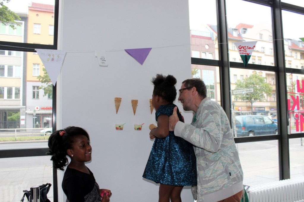 Ein Besucher hält ein Mädchen in den Händen und hilft ihr die Eiswaffel-Installation zu betrachten. Ein weiteres Mädchen steht daneben und redet.