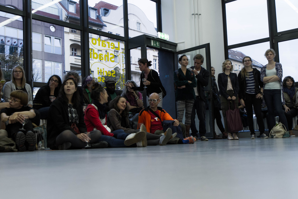 Zahlreiche Besucher versammeln sich im der Galerie vor den verglasten Wänden und verfolgen konzentriert die Performance.